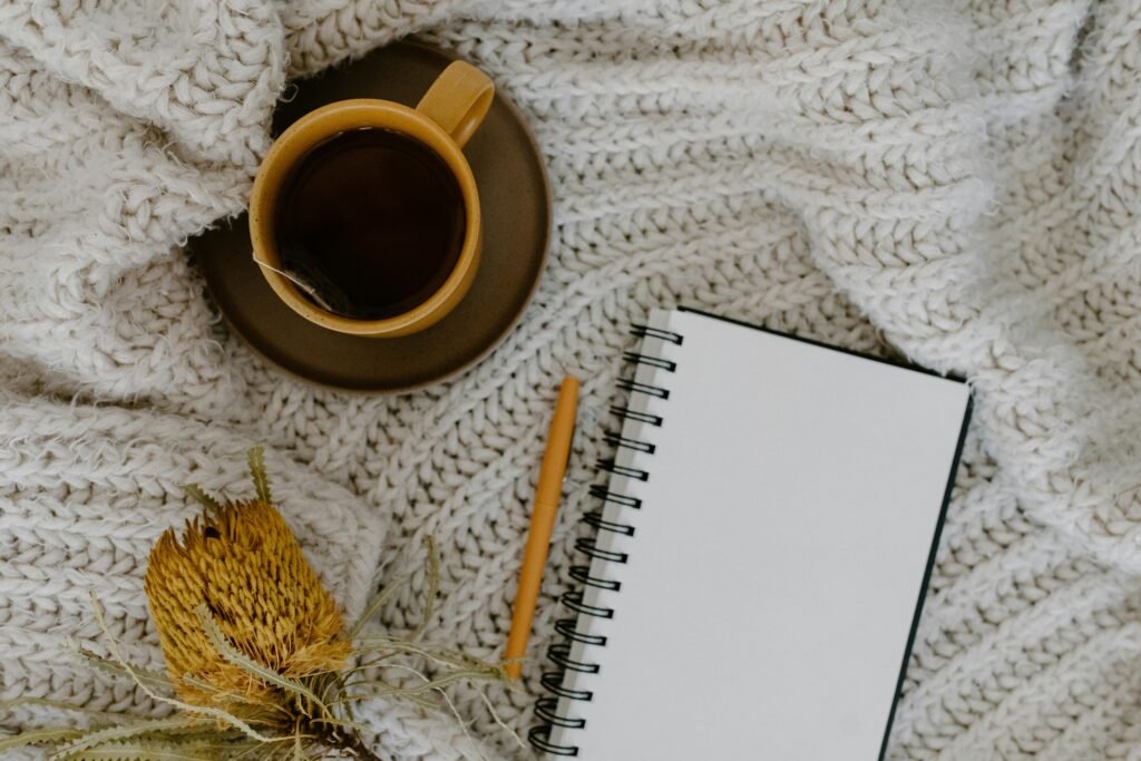 Warm flatlay with a cup of tea, a blank notebook, and pen on a knitted blanket.